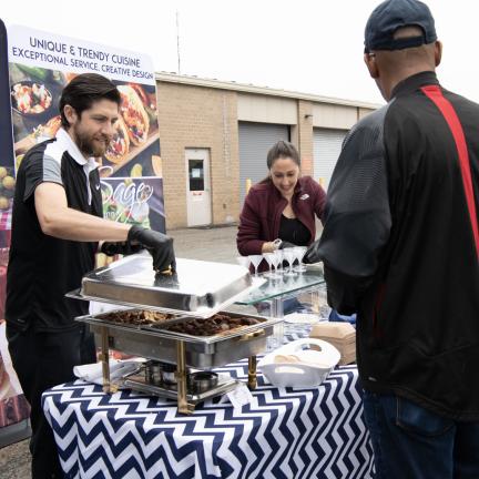 Photo: an individual standing at a catering table while happy caterers serve him